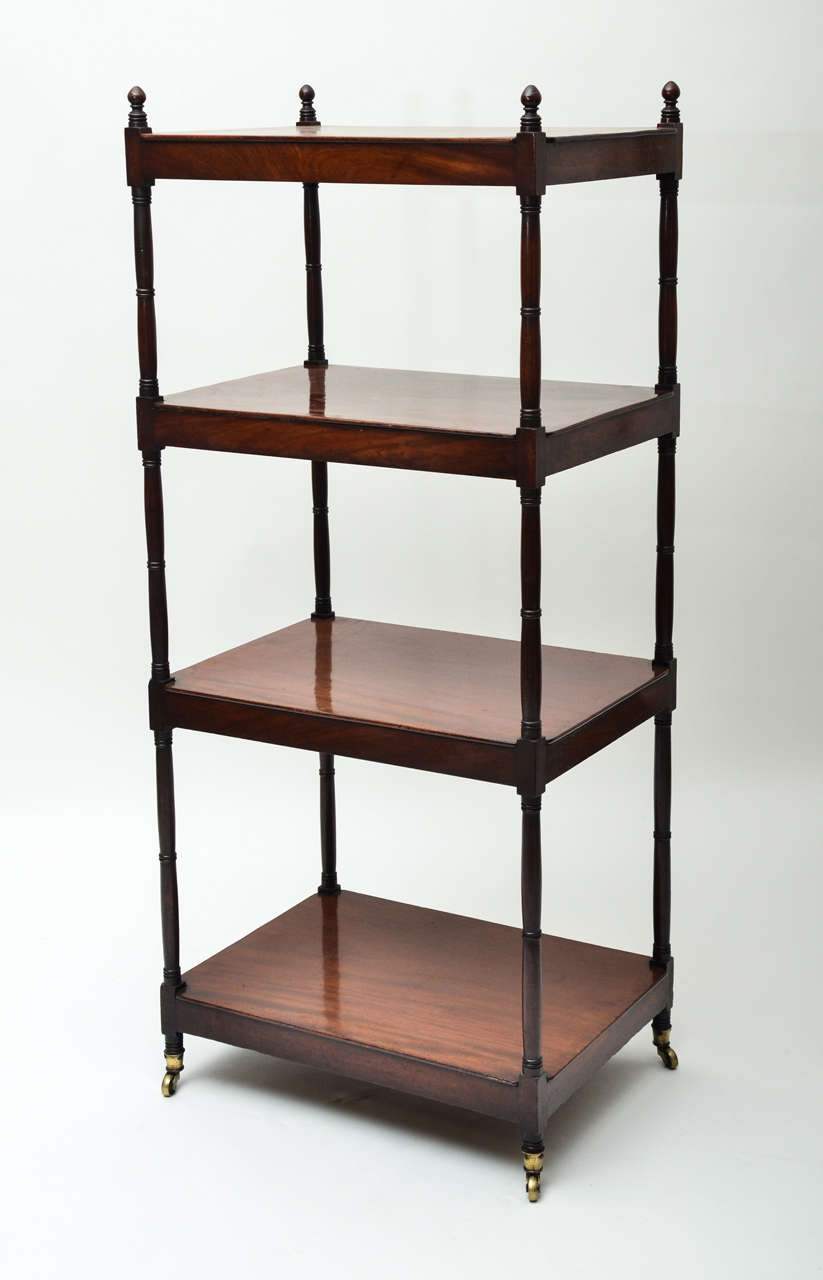 A 19th century four-tier mahogany étagère with unusually wide shelves, figured wooden finials, and original brass casters.