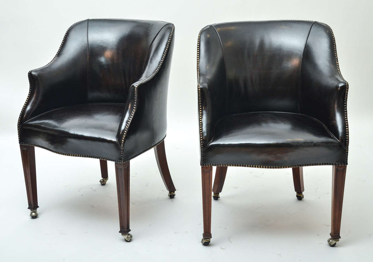A pair of leather upholstered chairs from the Carlton Club in London, brass studs, mahogany legs, and original casters. Two pair available. Perfect height for using as desk chairs.