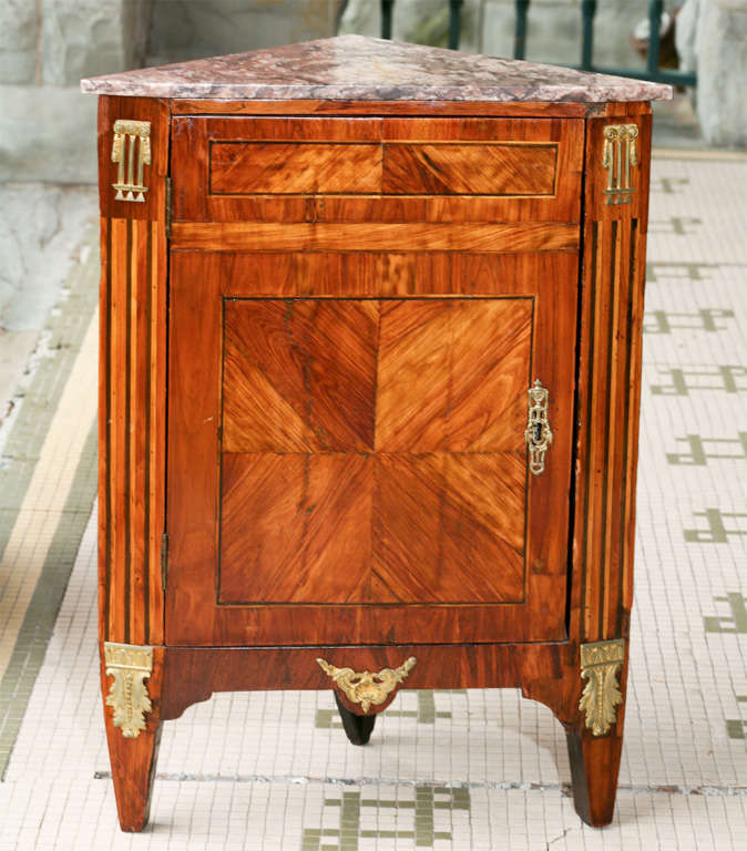 This fine and small Enconignure (corner cabinet) is constructed of book-matched and quarter paneled Tulip-wood veneer bordered by marquetry line inlays and marquetry stop fluting at the corners. All of this is enhanced with gilt bronze mounts