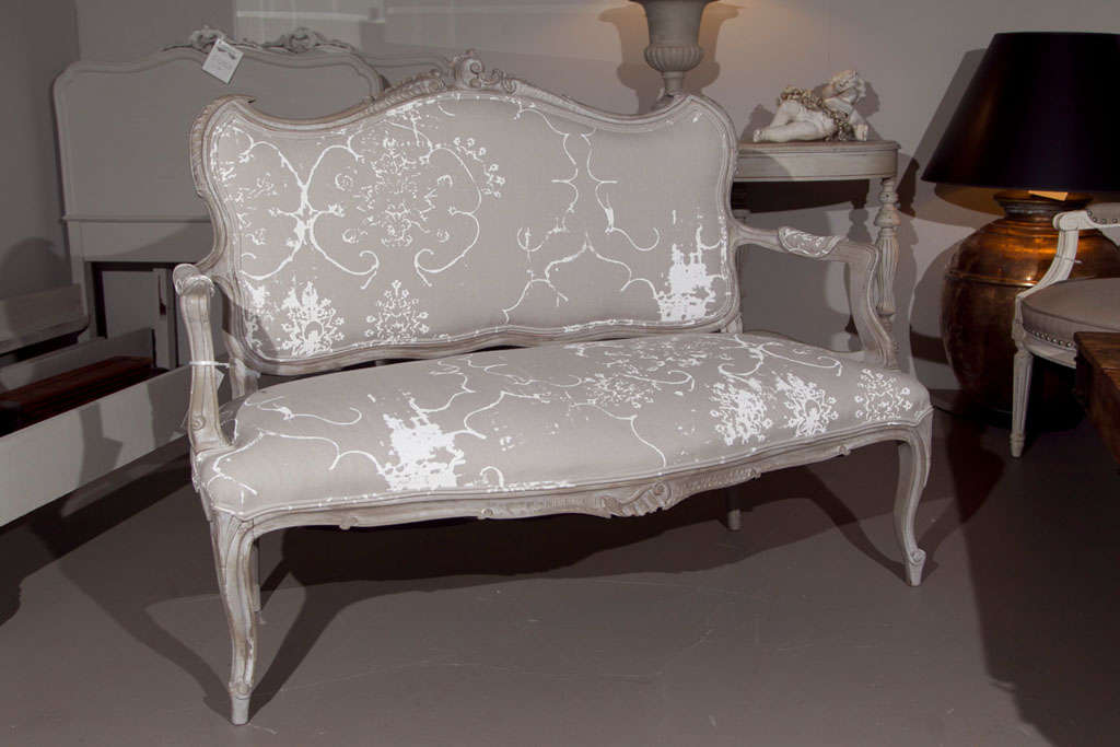 A gris-peinte French Rococo style settee, the shaped back with scrolled crest, padded back, armrest, and seat, new upholstery.