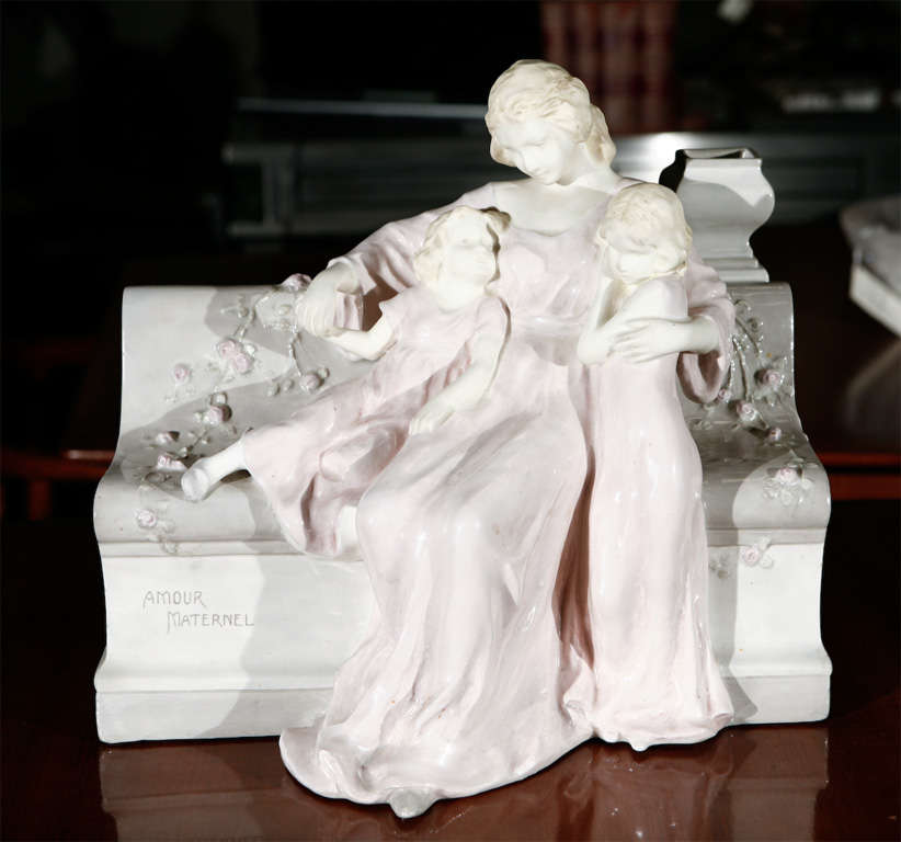 A Vienna faience porcelain figurine representing Motherly Love by Schauer. Bench and figures are porcelain. Faces adn arms are in a bisque (flat) finish. Marked on the bottom Vienna Faience Schauer. Also impressed on the bottom 