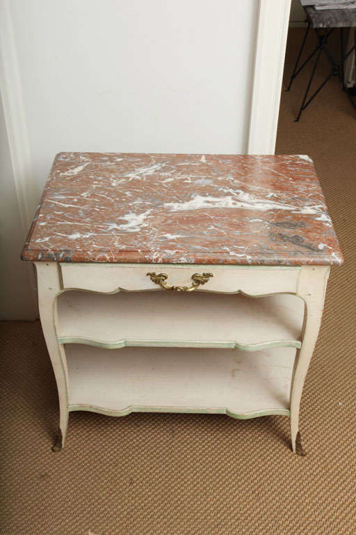 A Louis XV Style Gilt Metal Mounted Painted Side Table with a Molded Brown and Gray Marble Top. One Drawer and Too Serpentine Shelves on Cabriole Legs with Sabots
Provenance Frederick P. Victoria, From the Estate of Brooke Astor