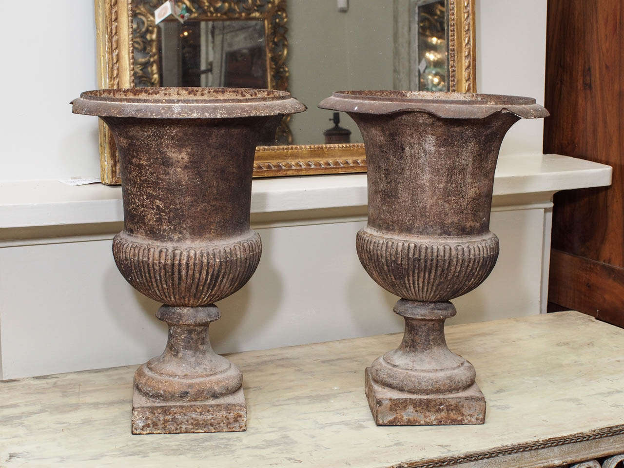 A pair of iron Campana form urns, elegantly rendered, with finely reeded or gadrooned detail on the lower body over a pedestal base.  Rims damaged.