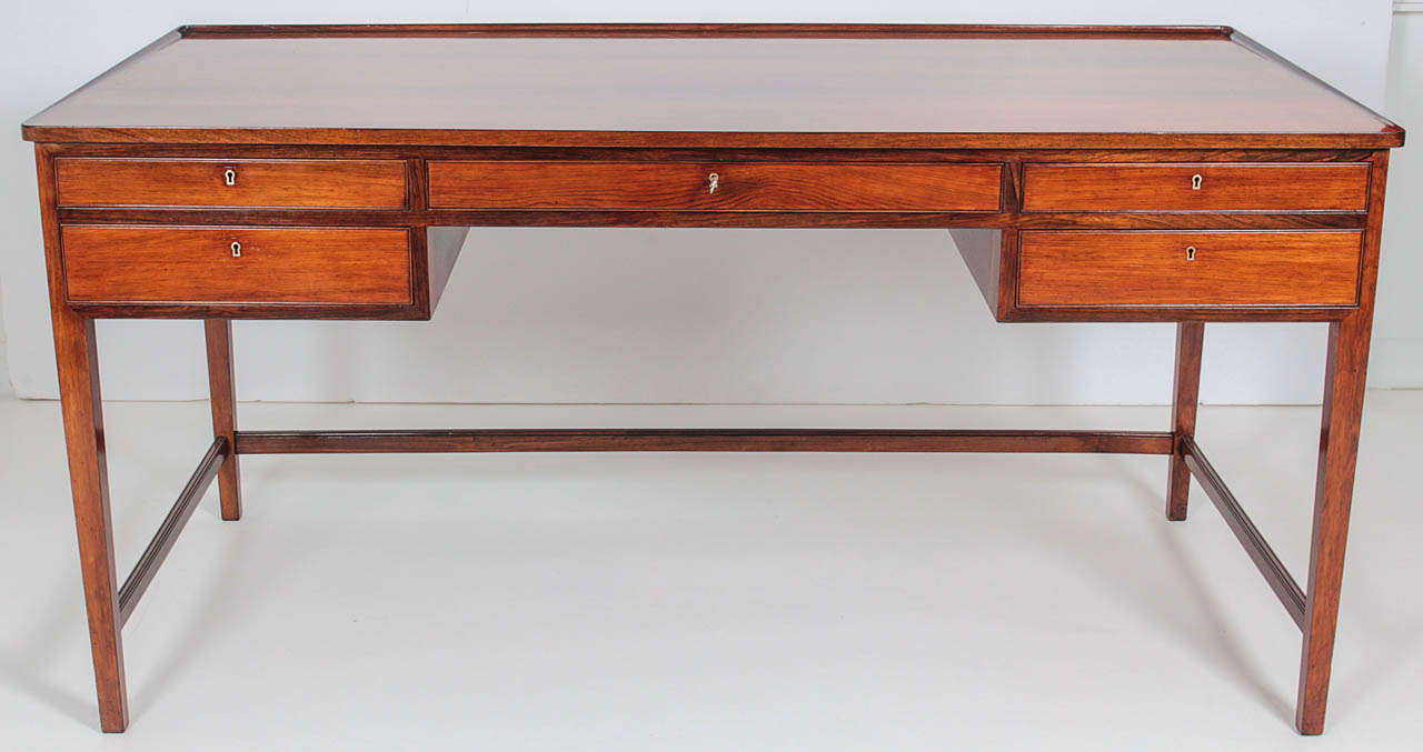 A Danish Modern rosewood writing desk, Circa 1950-1960s, the  a rectangular top with a subtle graduated lip on the sides and back edge, over s typical five drawer configuration raised on sqaure tapered legs with a three sided stretcher.