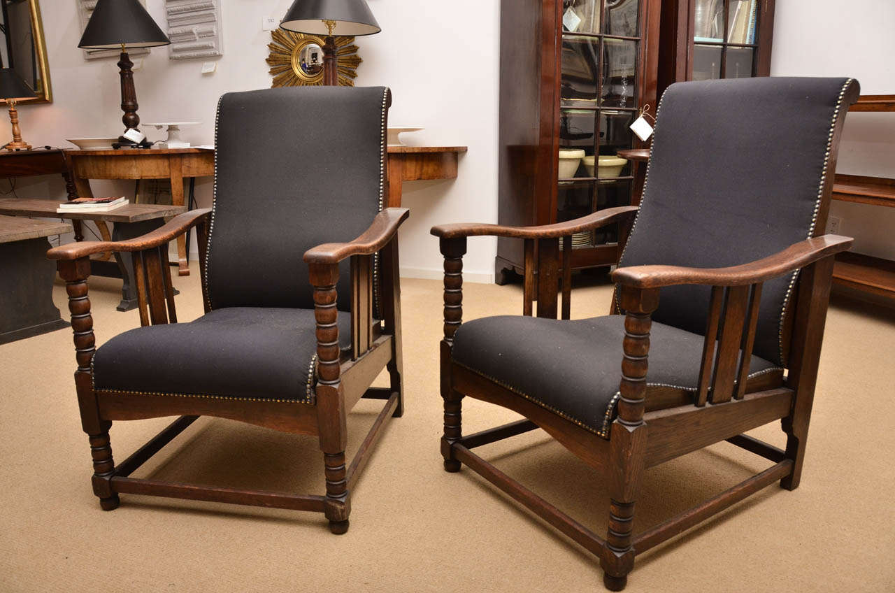 A pair of Arts & Crafts upholstered oak reclining chairs from the 1920's with bobbin turned front legs and sloping armrests with three slats.