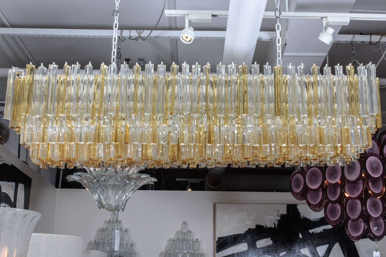 A unique and magnificent murano glass chandelier. Comprised of individually hand blown murano glass triangular (triede) crystal prisms in alternating colors of gold/amber and clear on a white streel frame, this large mid century Italian chandelier
