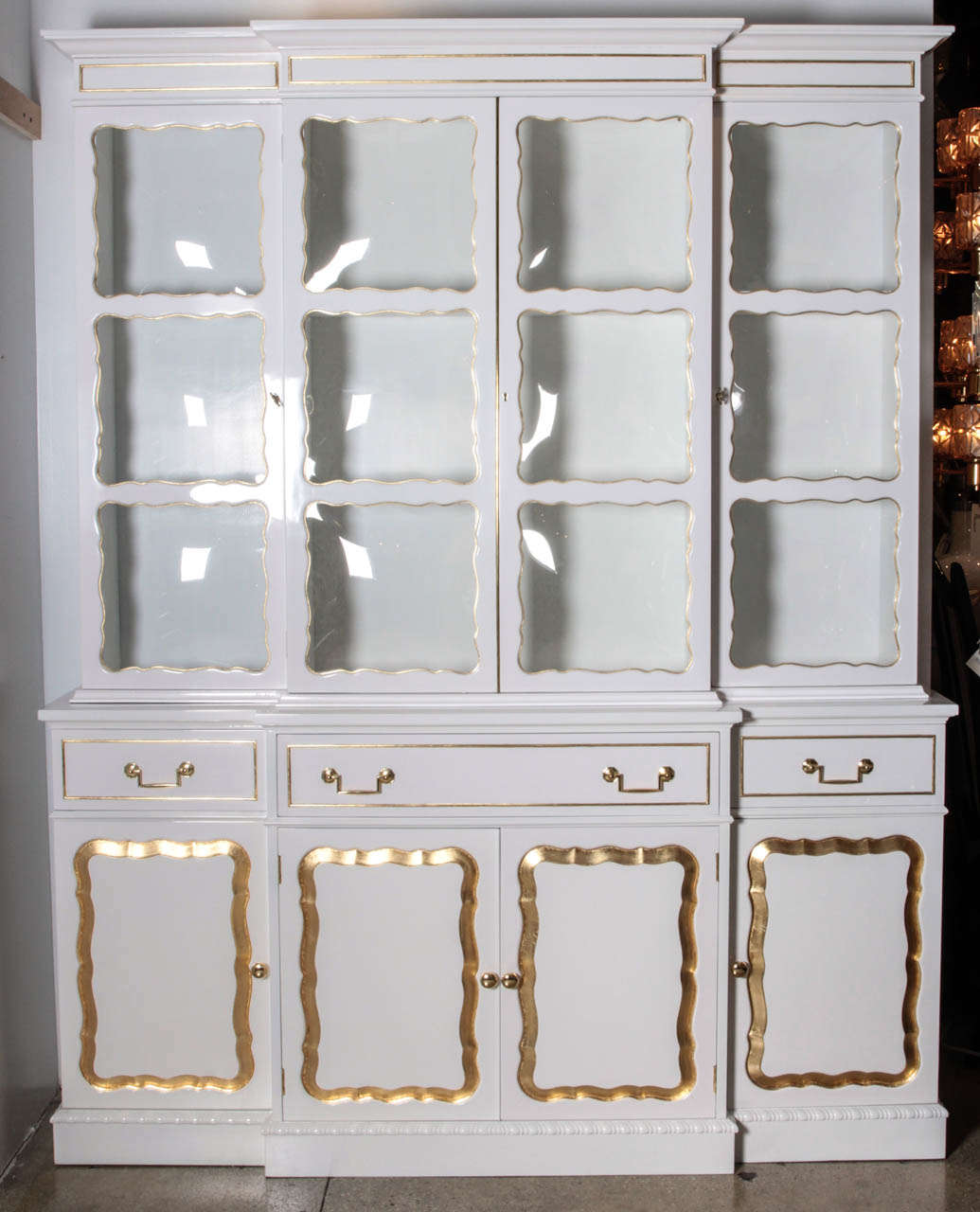 Ultra Glam Hollywood Regency white lacquer bookcase/breakfront with carved and 22kt gold leafed trim.The  Middle section folds down to reveal a secretary compartment and writing surface. Upper case features gilded trimmed convex glass window panes.