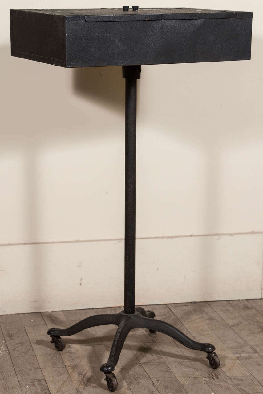 Black painted metal makeup case on wheeled stand.