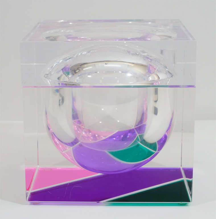 A vintage cube-form Lucite ice bucket with a swivel lid and spherical interior. The piece has pink, purple and green detailing on the bottom.