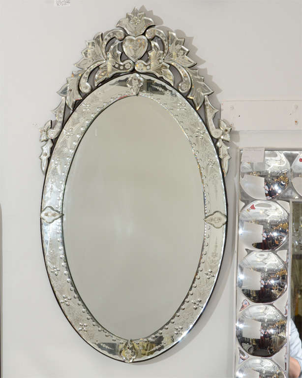 A vintage oval Venetian wall-mounted mirror with elaborate scrolling  framing a heart on the top