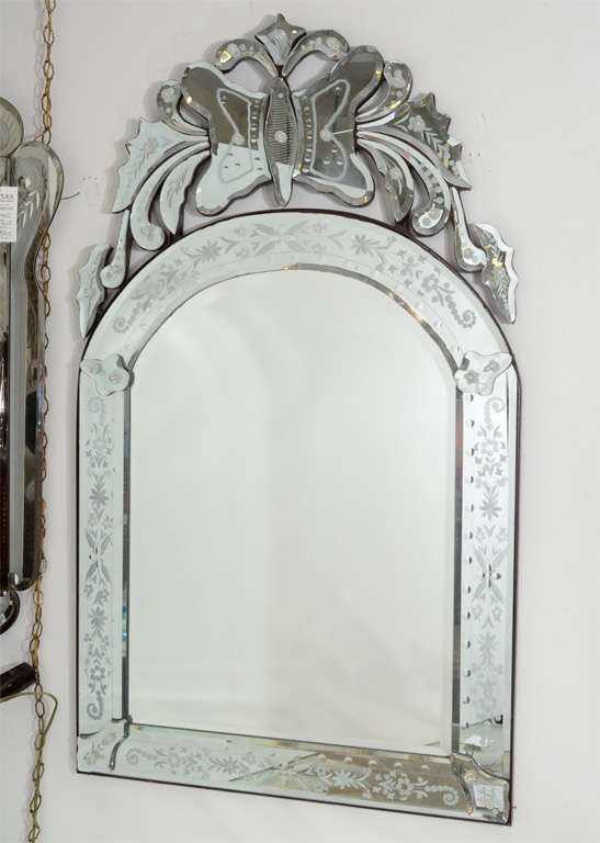 A vintage arched Venetian mirror with etched border and mirrored butterfly and acanthus detail on the top. The piece has age appropriate wear; some scratches