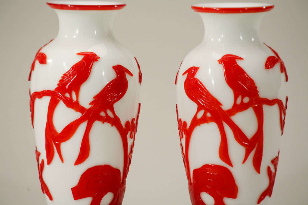 This striking pair of Chinese Peking Glass vases have age and great quality. The vases are cased in a vibrant red and cut back to reveal the white ground color. This glass is made of two layers with the well-carved outer layer of birds, flowers and