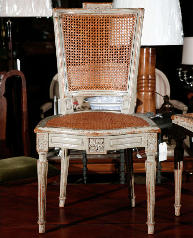 A good set of eight French Louis XVI style dining chairs, circa 1900. Each chair has a cane seat and back with worn painted surfaces. Note the nicely carved embellishments on the turned, fluted legs and the shaped backs and seats. 