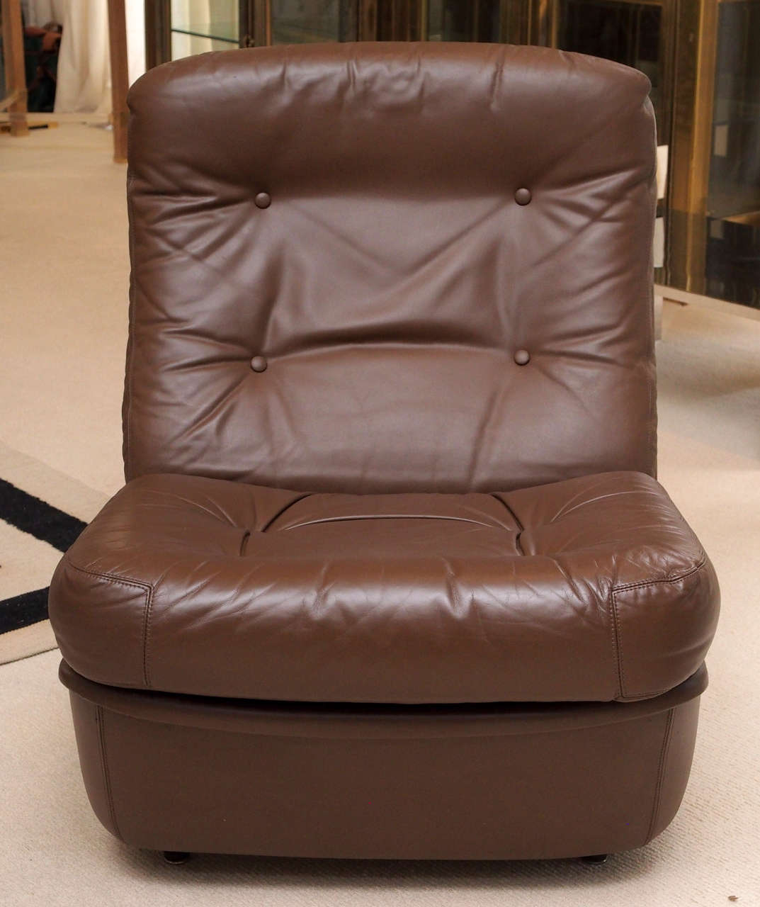 Two low armless lounge chairs by Airborne, so labelled; with tufted cushions, fixed at the back, loose at the seat; casters at the rear; three additional chairs available.