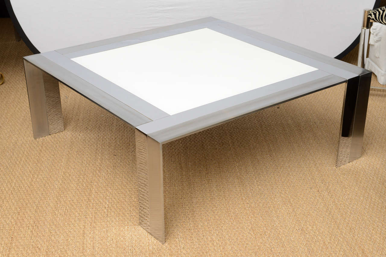 The wonderful mixed composition of brushed versus high polished stainless steel in this chic cocktail table has a square pieces of white fired glass in the center.
This table is extremely heavy and well-made. The juxtaposition of the two ways of the