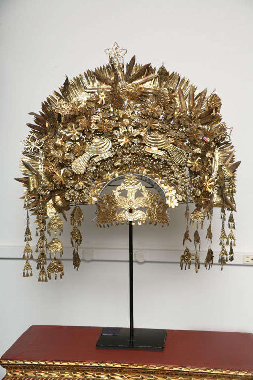 A ceremonial wedding headdress.  Adorned with arrayed layers of golden metallic trinkets.  On a stand.