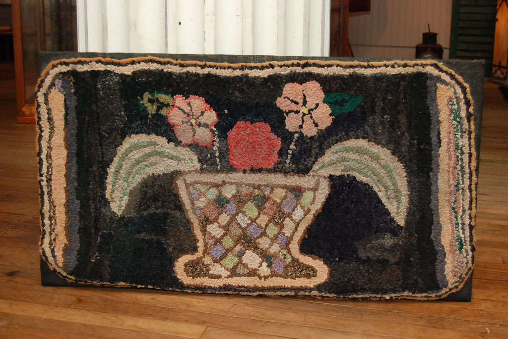 early hooked rug of a basket of flowers<br />
hooked with strips of early fabrics<br />
attached to a rectangular wall board for hanging