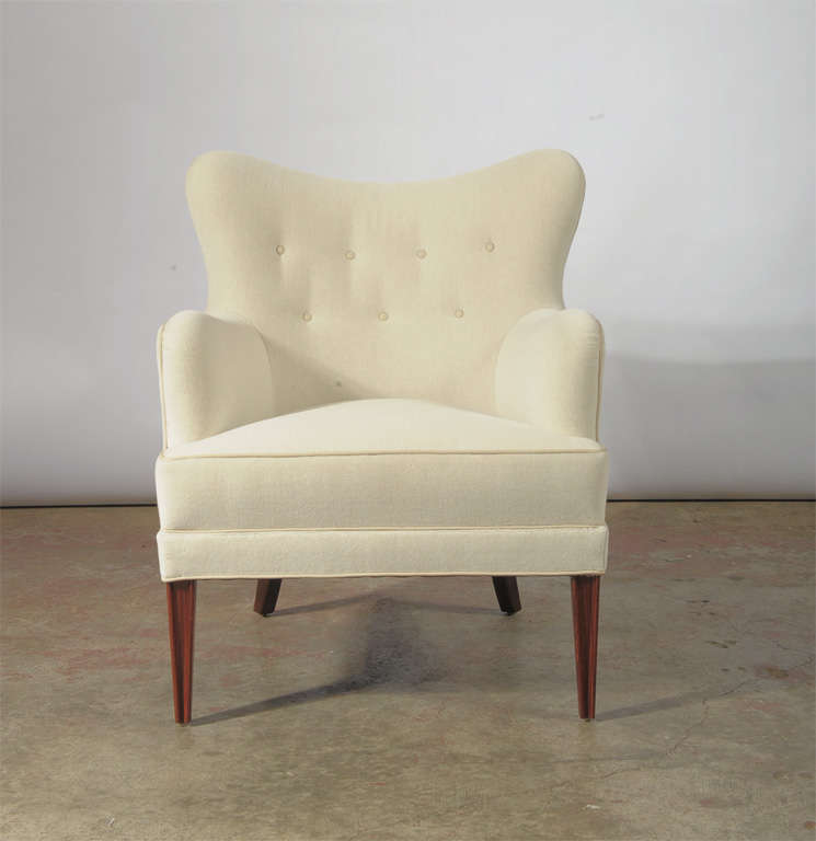 A custom wing back chair inspired by Nordic modern design, which can be made with a variety of wood types, and can be covered in leather or fabric. (Photographed in Maharam Alpine white velvet with white leather buttons and piping, and Mahogany