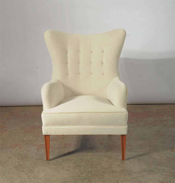 A custom wing back chair inspired by Nordic modern design, which can be made with a variety of wood types, and can be covered in leather or fabric. (Photographed in Maharam Alpine white velvet with white leather buttons and piping, and Mahogany