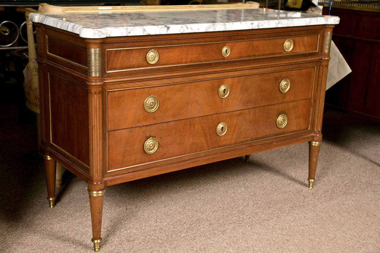 French mahogany marble-top commode in the Louis XVI style, circa 1940s, the white and grey veined marble-top a banded frieze fitted with a long narrow drawer, flanked by bronze mounts, over two large drawers decorated with brass loop pulls, raised