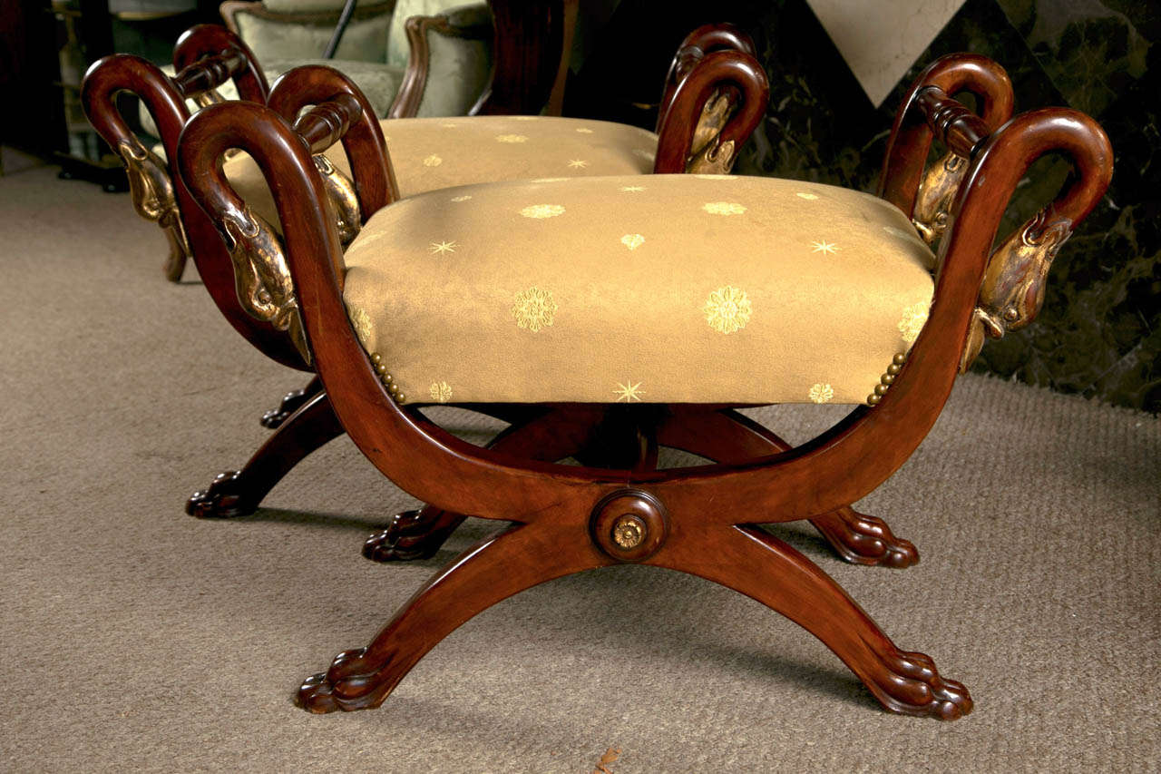 Pair of spectacular French neoclassical style walnut benches, each decorated with parcel-gilt swan head motifs, upholstered in embroidered golden fabric, overall in Curule form, raised on claw feet.