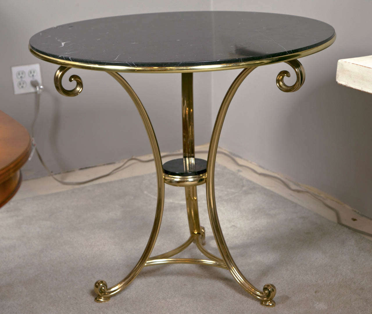 Art Deco style center table, the charcoal circular marble set in a gilt-brass banding, supported on scrolled uprights joint by a lower tier and a triangular stretcher, extending to scrolled toes.