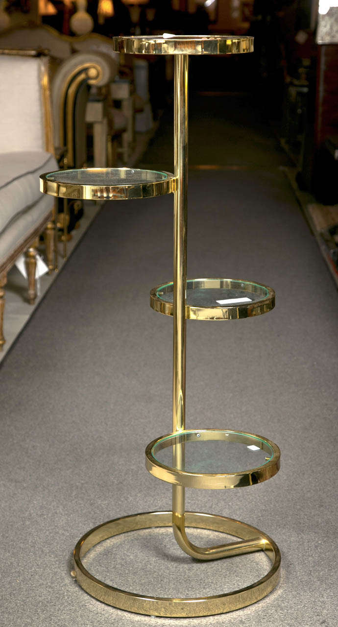 A brass mid-century four tier glass plant stand pedestal. The circular base supporting four glass shelves. All on a brass base.