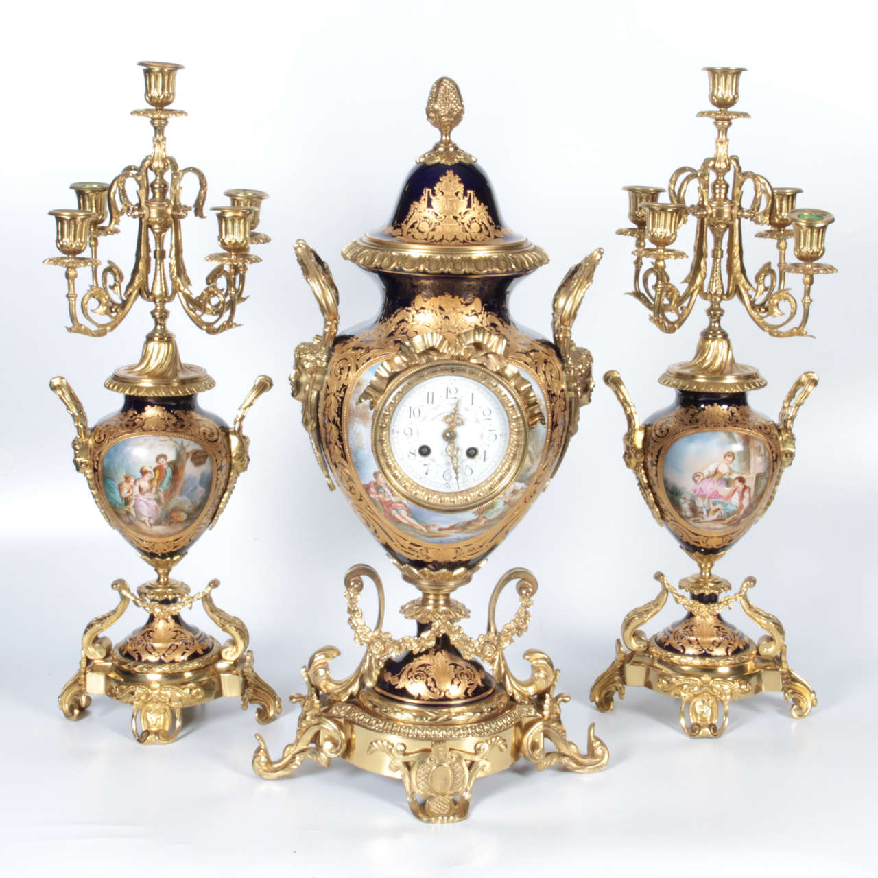 A beautiful antique French ormolu-mounted royal cobalt blue sevres porcelain three-piece clock garniture accompanied by the original pair of five-light candelabrum, 19th century. There are pastoral scenes in the vein of Boucher decorating the