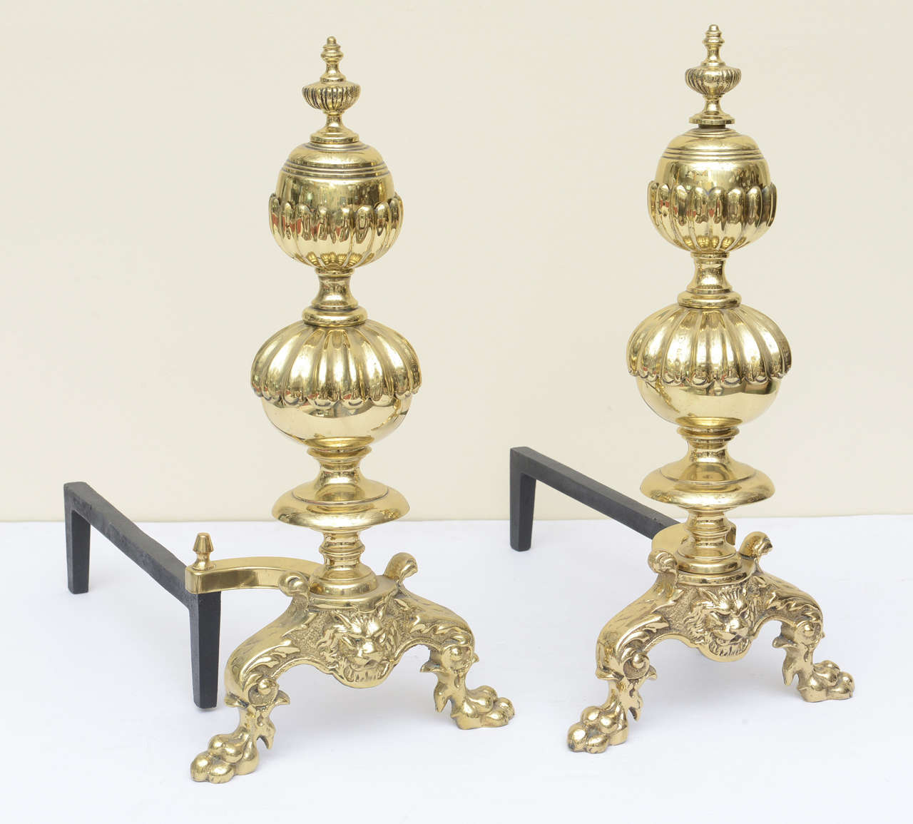 Monumentally oversized Georgian style andirons, solid brass plated, with lion-footed feet and lion head motif, with tiered, fluted bulbous middle extended to the large acorn-like finial tops, and capped tops.