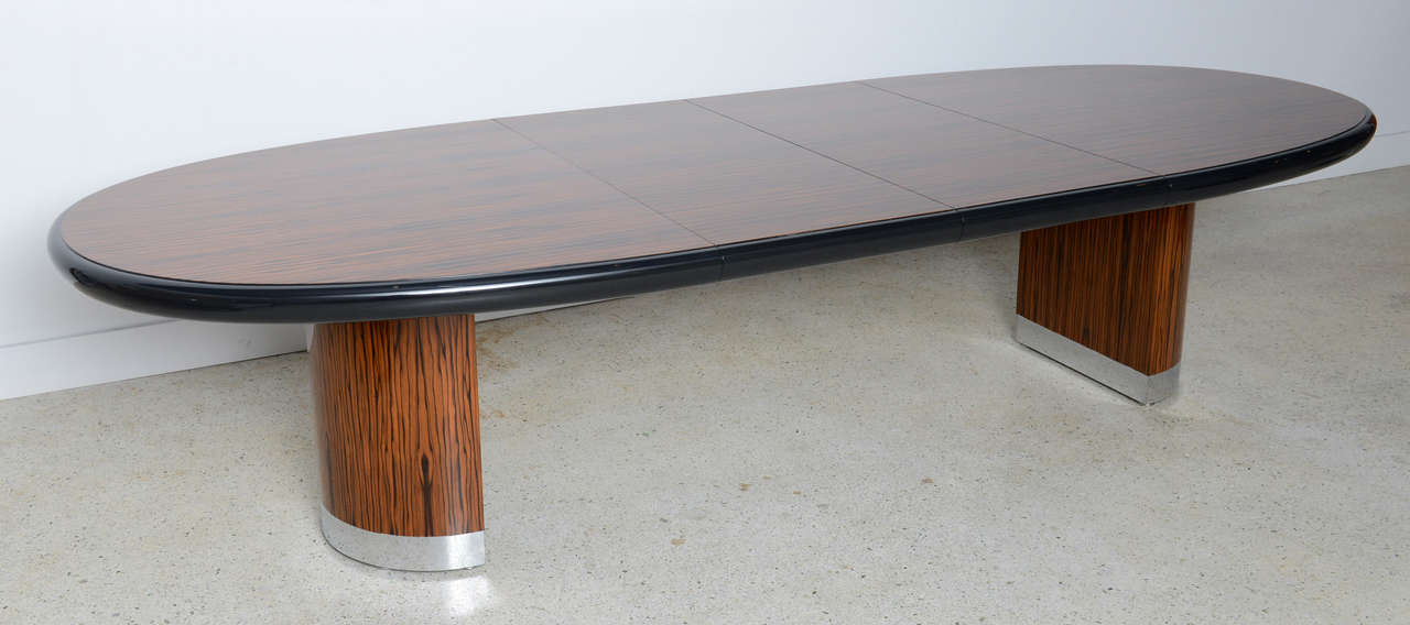 The oval top in zebra wood banded in black lacquer, the top to accommodate two leaves, on demilune bases banded in chrome, Kagan or Dreyfuss label to underside.