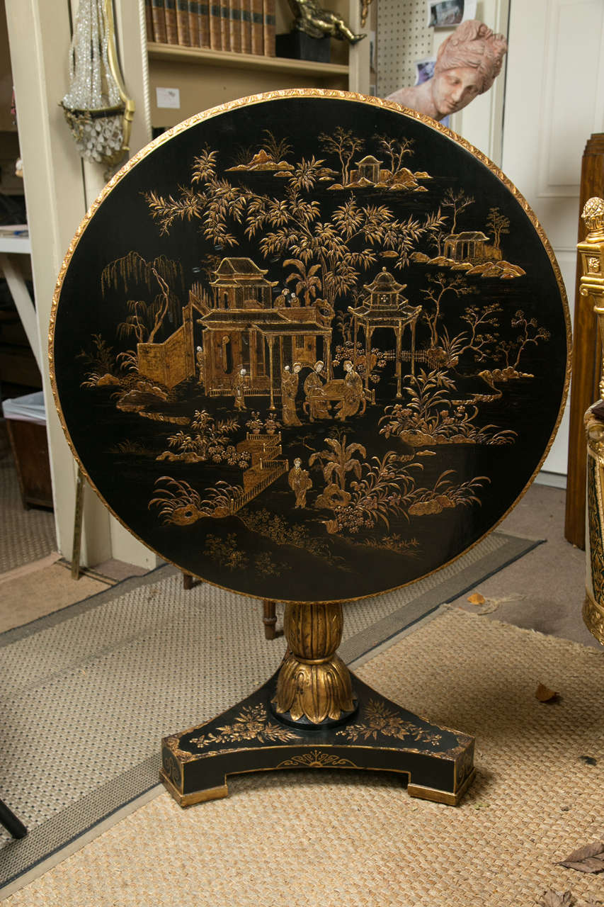 This table is lacquered black and gold with Chinese scenes. The top has a gadrooned edge. The pedestal with gilt decoration, as is the tripartite base.
