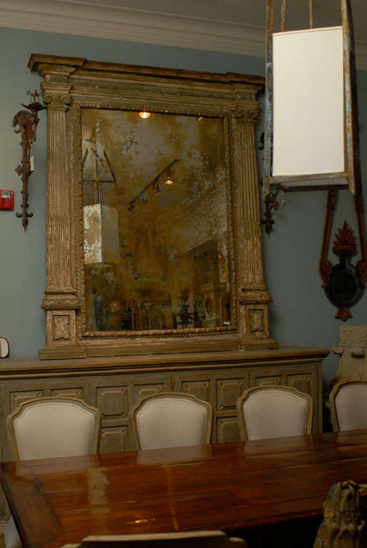 A very large 18th century carved and painted Italian mirror. 

This spectacular Italian mirror of very large size is flanked by two fluted pilasters topped by voluted capitals. The mirror features a profiled molding and a new antiqued mirror has