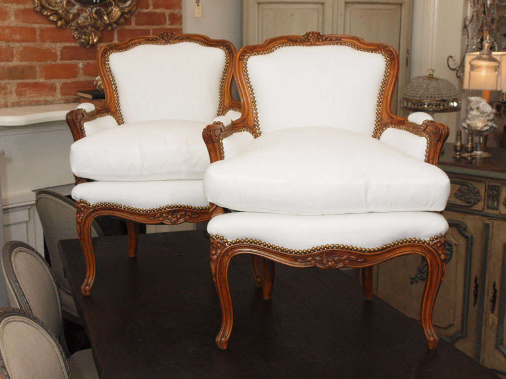 Completely restored walnut Louis XV Bergeres, retied springs, all hand tied.  Reupholstered in a white Belgian linen with french brass nailhead trimming and a soft down wrapped cushion.  Cabriole legs and hand carved frame.  Absolutely breathtaking.