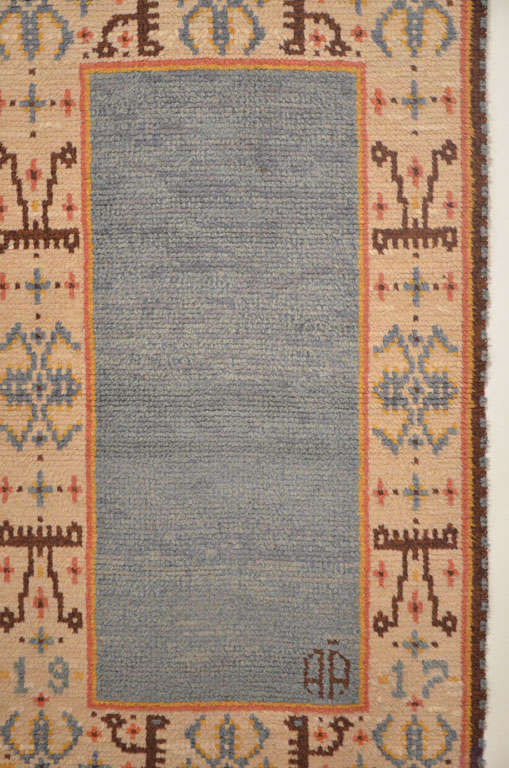 An unusual hand-knotted Rya rug, dated 1917 and signed AA, with a sky blue open field framed by an ivory border decorated by geometric devices typical of Swedish Folk Art. Weavings such as these are often found in excellent condition because they
