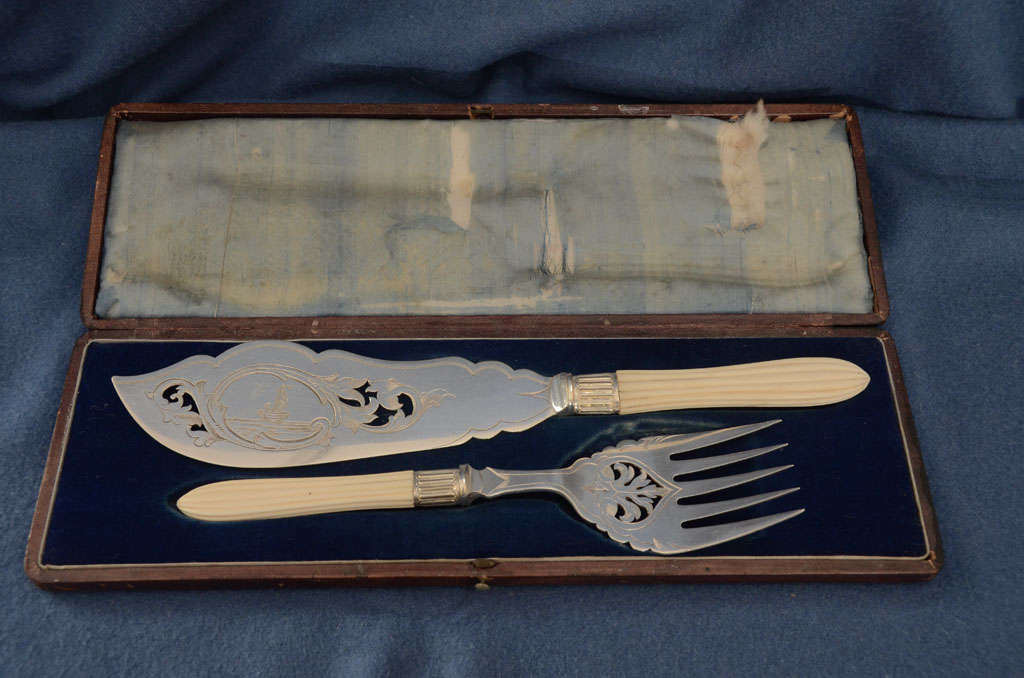 ENGLISH SILVER PLATED FISH SERVING KNIFE & FORK WITH CUT OUT FOLIATE DESIGN--- ENGRAVED SAILING BOAT TO KNIFE--IVORY HANDLES WITH RIBED CARVING--WITH ORIGINAL BOX--KNIFE 12.5 LONG--FORK 9