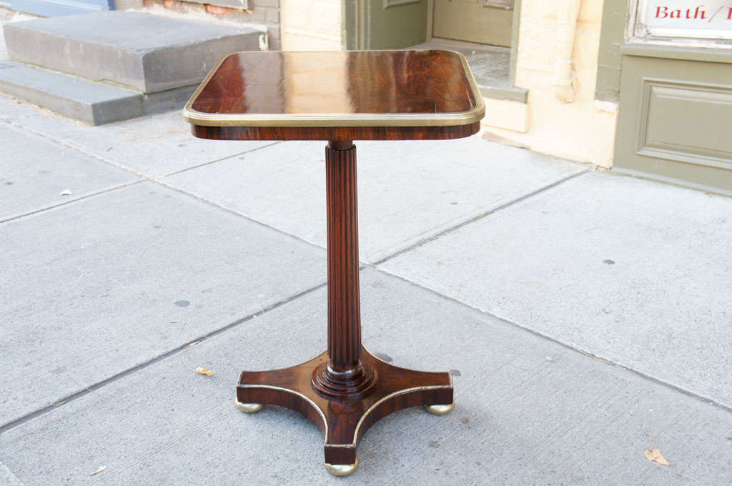 This fine piece of furniture is made from rich deeply grained rosewood. Even the pedestal support is turned and carved from solid rosewood. The table is further accentuated with a wide brass band around the top and delicate decorative brass trim