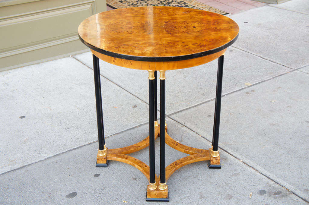 This Fine Baltic center table in burled elm has ebonized and water gilded decorative elements creating a simple yet refined table.  The use of double columns and the open work lower stretcher makes the table light in feeling while the black keeps it