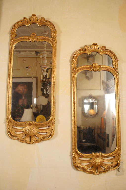This fine pair of mirrors are completely done in carved and gilded wood. Executed in the Rococo taste the mirrors are a combination or S and C scrolls creating movement and asymmetry. The pair has finely carved wood decorative elements that are