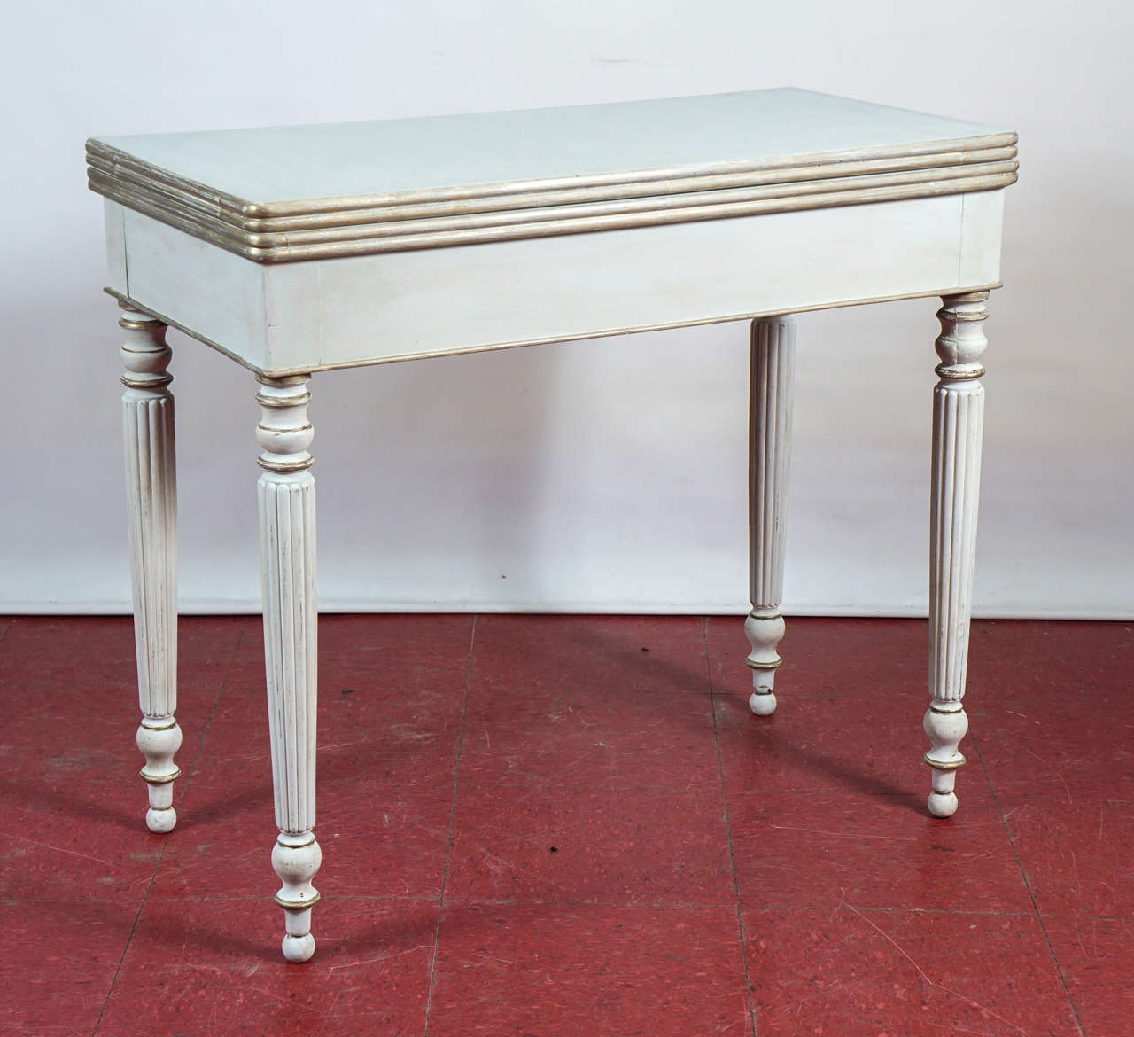 Set against a wall as a console or lamp table, the top unfolds and the back legs slide to fully support the unfolded half of a square card table, seating four players comfortably. The wood is mahogany painted white with gilt trim. Fluted and turned