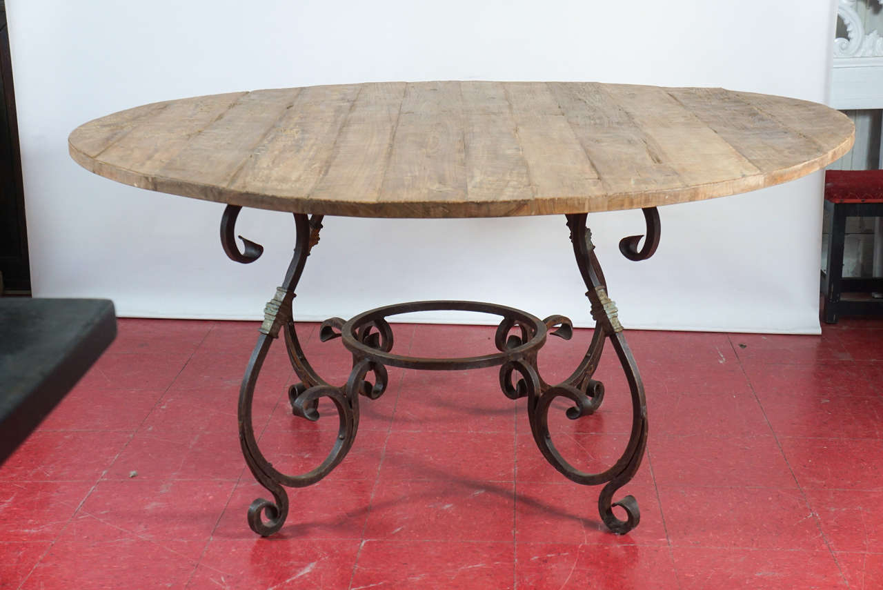 This rustic and elegant French Baroque style iron and teak wood round garden dining table can be used indoor or outdoors. The top made with reclaimed teak wood, thick scrolled hand forged iron base with a rust finish and some gilt. Excellent