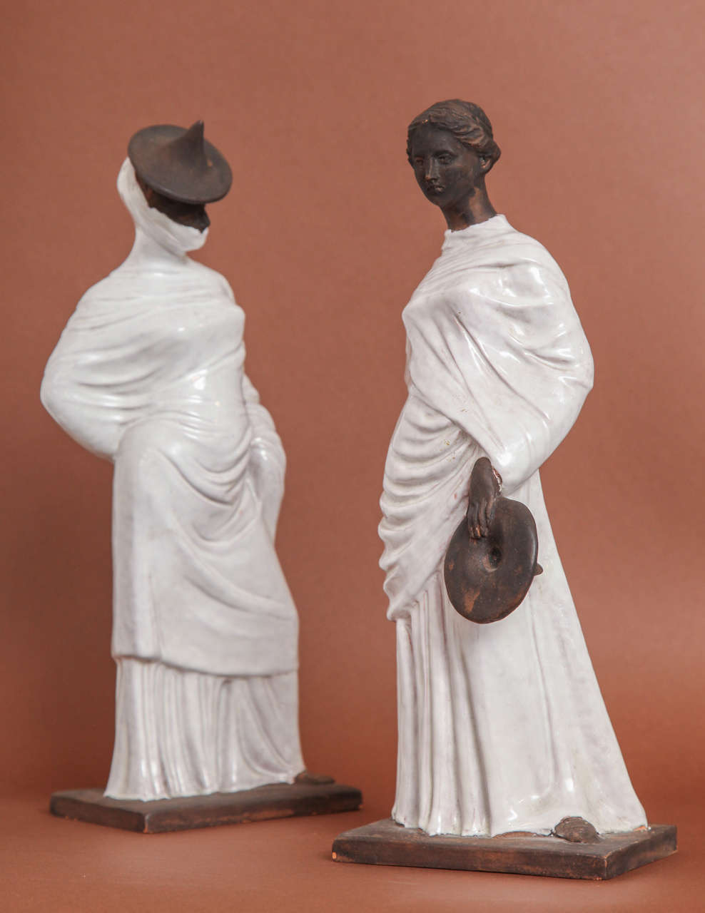 Two terracotta female figures dressed in white glazed folds of draped fabric.
Marked on bottom 