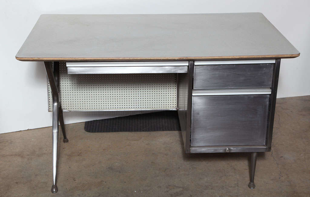 1950s Raymond Loewy for Brunswick Furniture Co. Steel desk with modesty perforated hardboard panel. Industrial desk contains three metal pull drawers including file cabinet drawer with a pale gray Micarta top and X designed support legs.