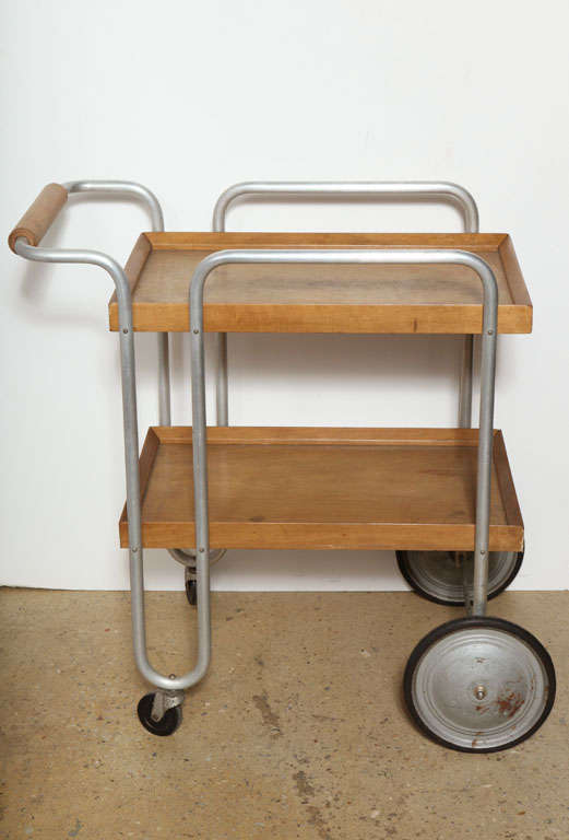 Rare Bauhaus Era rolling Birch and Aluminum Serving Cart. Featuring two Birch trays with Maple stain, an open and curved tubular Aluminum framework, cylindrical Birch handle, two large Aluminum detailed wheels with two smaller swiveling back