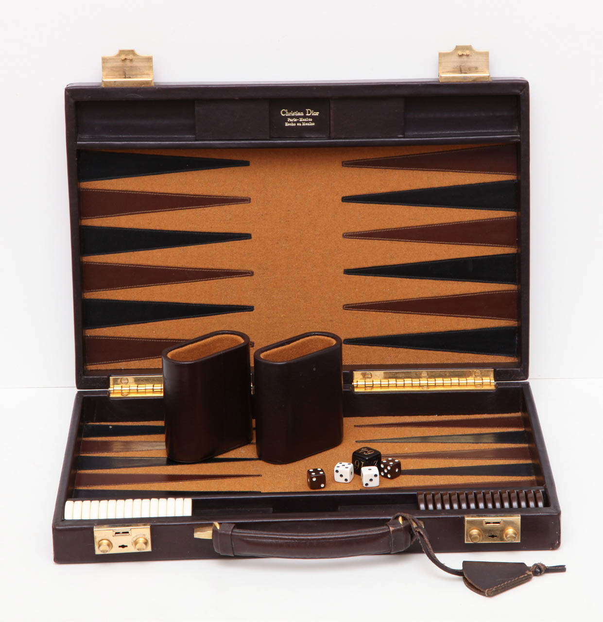 A vintage Christian Dior backgammon set in a Dior logo leather case with brass fittings. The game contains the original pieces including two leather cups.