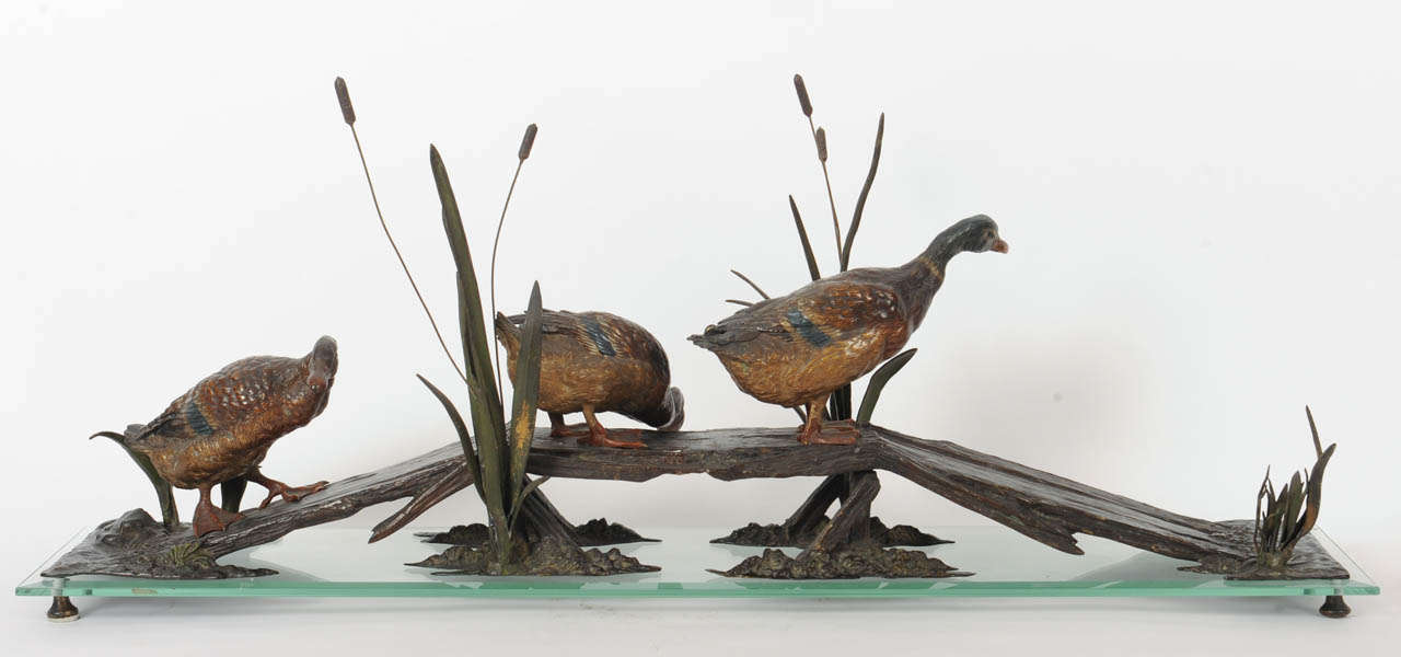 cold patinated bronze on a cut glass base

Striking Vienna naturalism. With a waggling walk three ducks cross a small pond over a bridge. It’s the technique of the polychrome colours that create a very realistic effect. This unusually large and