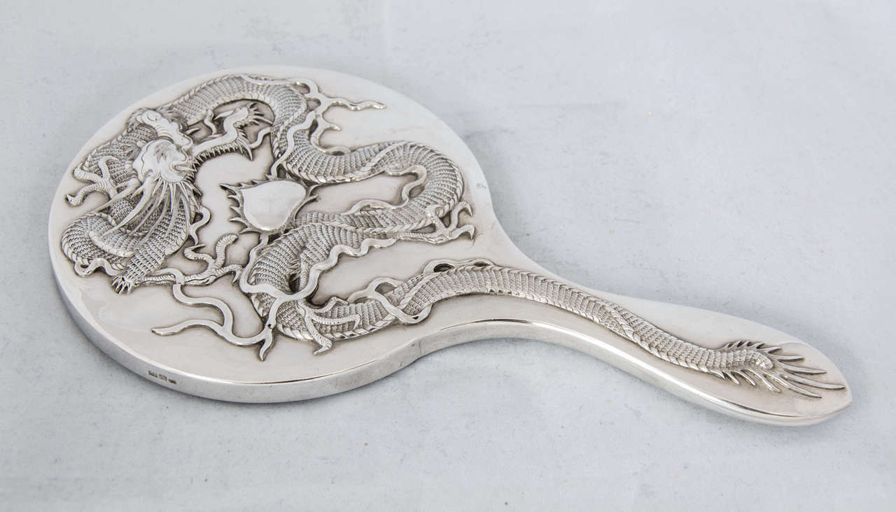 A Chinese Export Silver Hand Mirror applied with a beautifully detailed dragon on a plain background.
Maker's mark of 