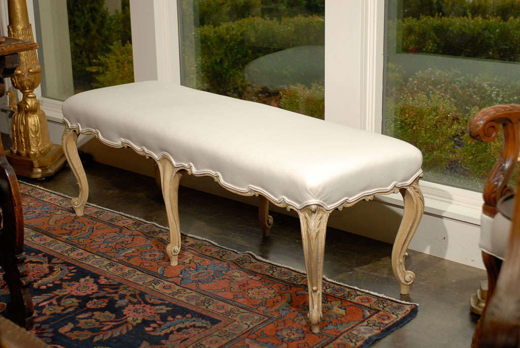 This elegant Louis XV style wooden bench from the turn of the century (19th-20th century) features a muslin upholstered seat resting on a nicely scalloped skirt. The ensemble is raised on six exquisite cabriole legs. The knees on the corner legs are