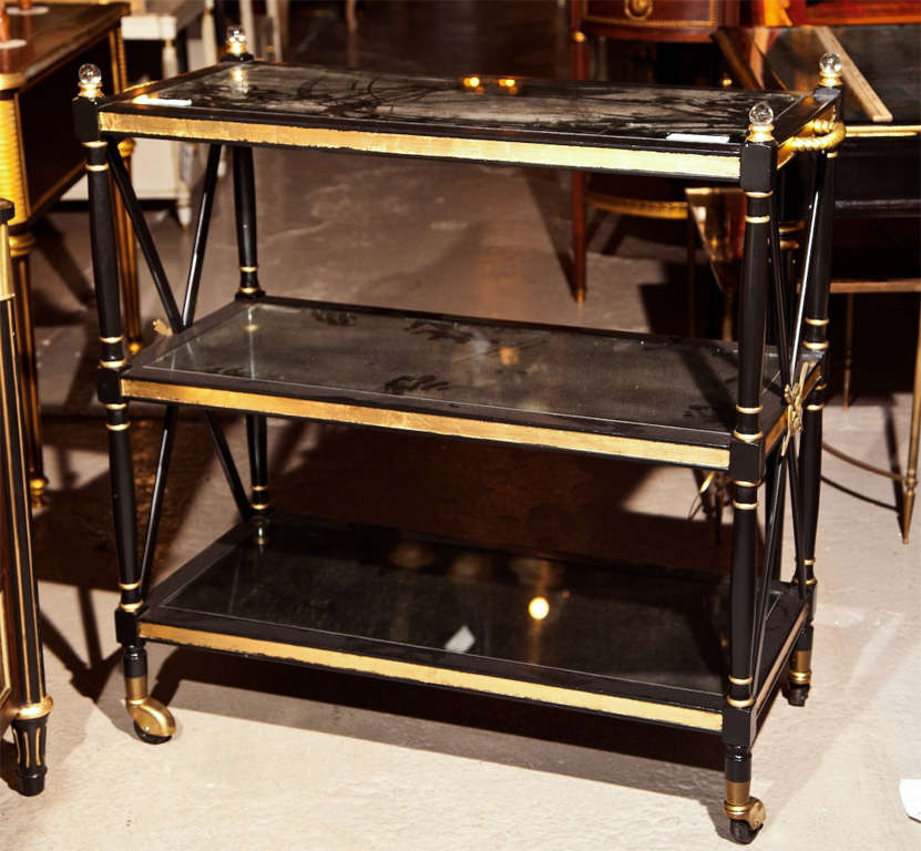 French Directoire style ebonized 3-tier serving cart, circa 1940s, overall ebonized with parcel-gilt decoration. Each shelf has antiqued glass top, the top shelf with bronze twisted handles on the side and four glass finials, X-form decoration on
