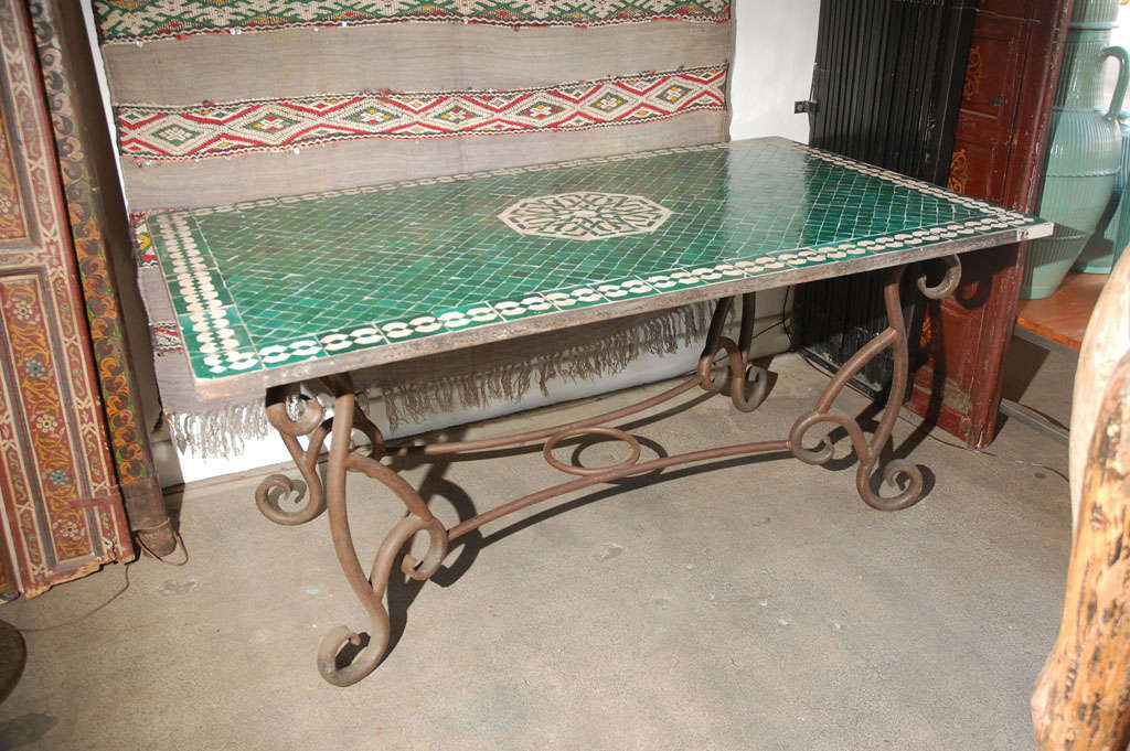 Gorgeous vintage Moroccan handcrafted tile table. Green glazed tiles incised designs in the middle and on the sides. The top table has a whole for the umbrella. Heavy wrought iron base in French Provence style.

We specialise in rare 18th and 19th