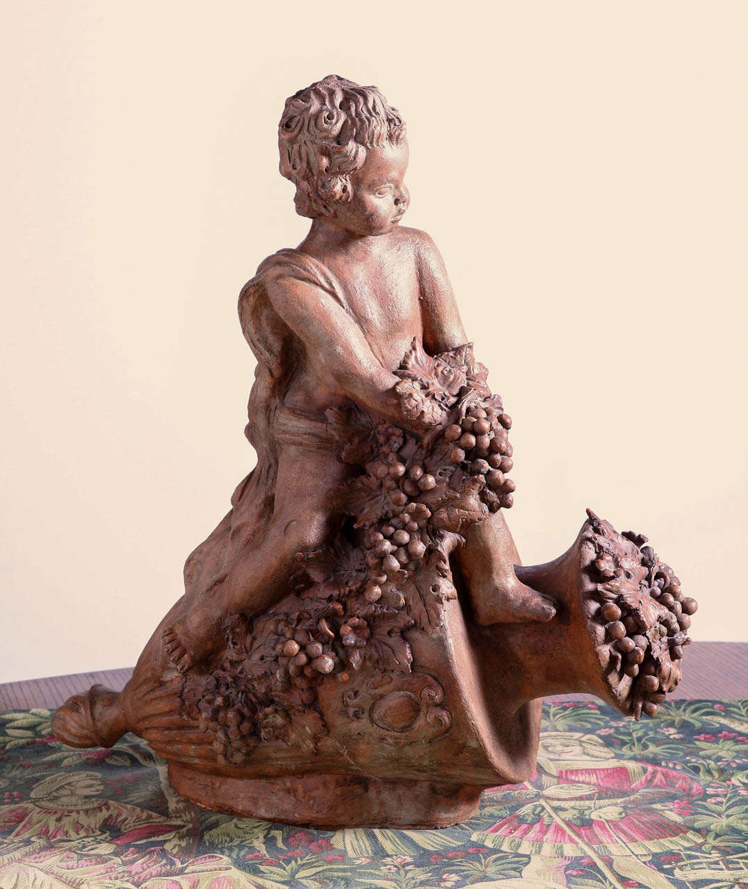 This antique French statue has been made from terra cotta clay.  It came from an old wine property in the Bordeaux region of France and dates to the mid 1800’s.  It depicts a Bacchanalian putti resting atop an urn on its side filled with grapevines